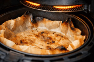 에어프라이어 바스켓 안에서 종이호일이 갈색으로 그을리고 열선 쪽으로 말려 올라간 모습