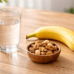 배고플 때 위 자극을 줄이기 위한 물 한 잔과 바나나, 견과류가 놓인 밝은 테이블 위
