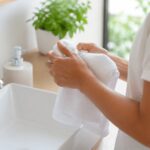 손 위생 관리를 위해 밝은 욕실 세면대 앞에서 깨끗한 흰 수건으로 손씻기 후 물기를 제거하는 장면